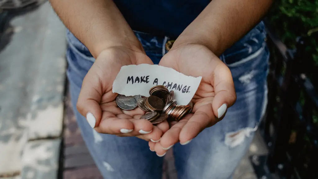 Outstretched hands hold coins and a paper note that says, "Make a change."