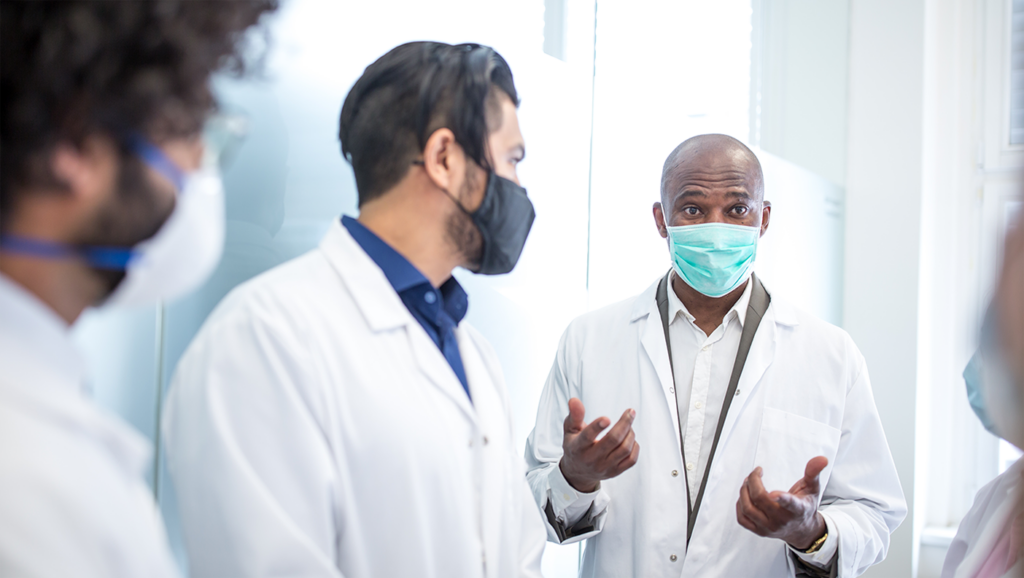 A picture of four doctors at a health organization having a conversation, all wearing masks.