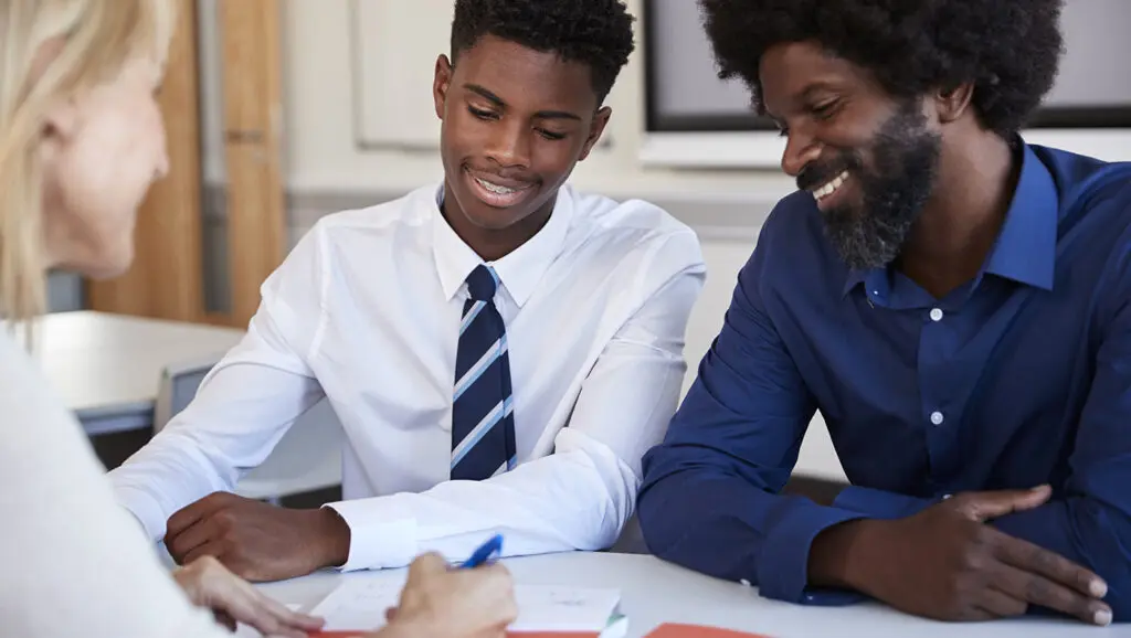 A picture of a parent and their teenager in uniform sitting at a table with an admissions officer at an independent school.
