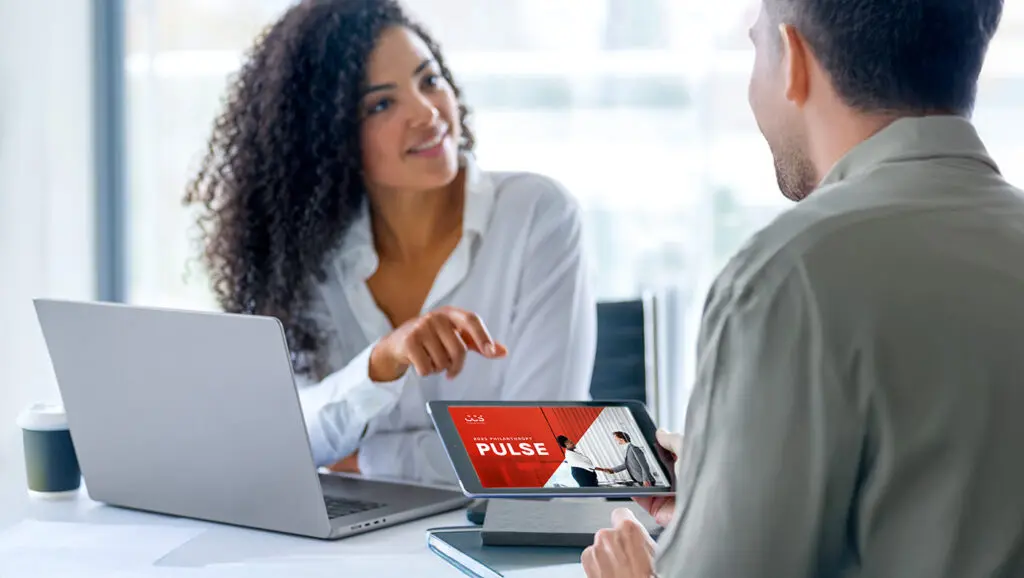 A picture of two nonprofit professionals sitting at a table as they view and discuss the 2025 CCS Philanthropy Pulse report on a tablet.