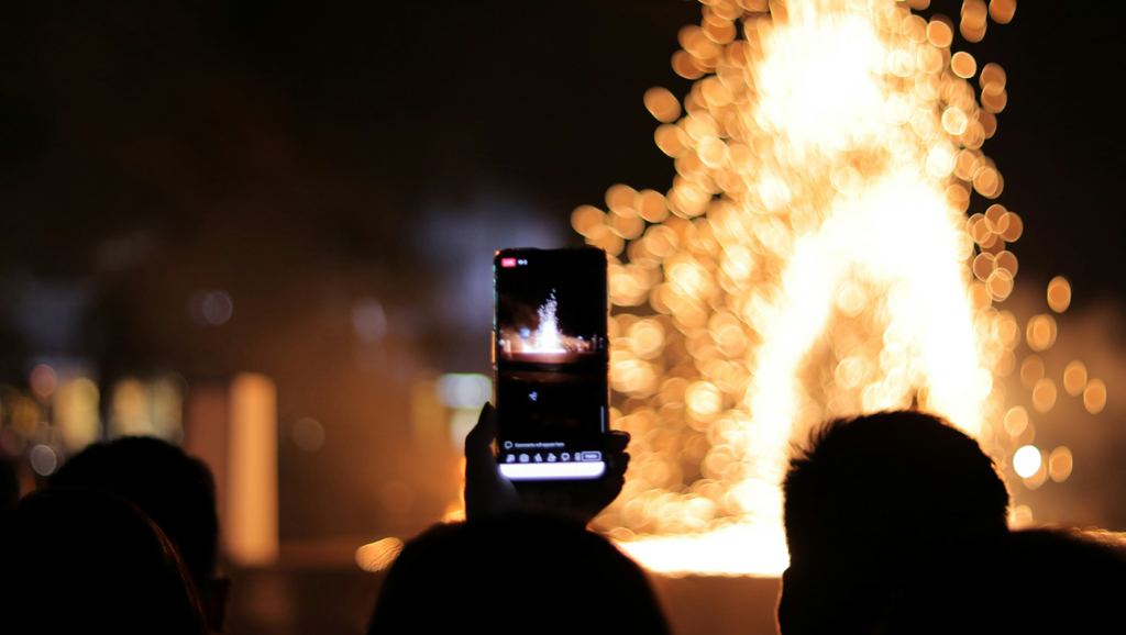 Fundraising event attendees hold up a phone as they record a light show outside at night.