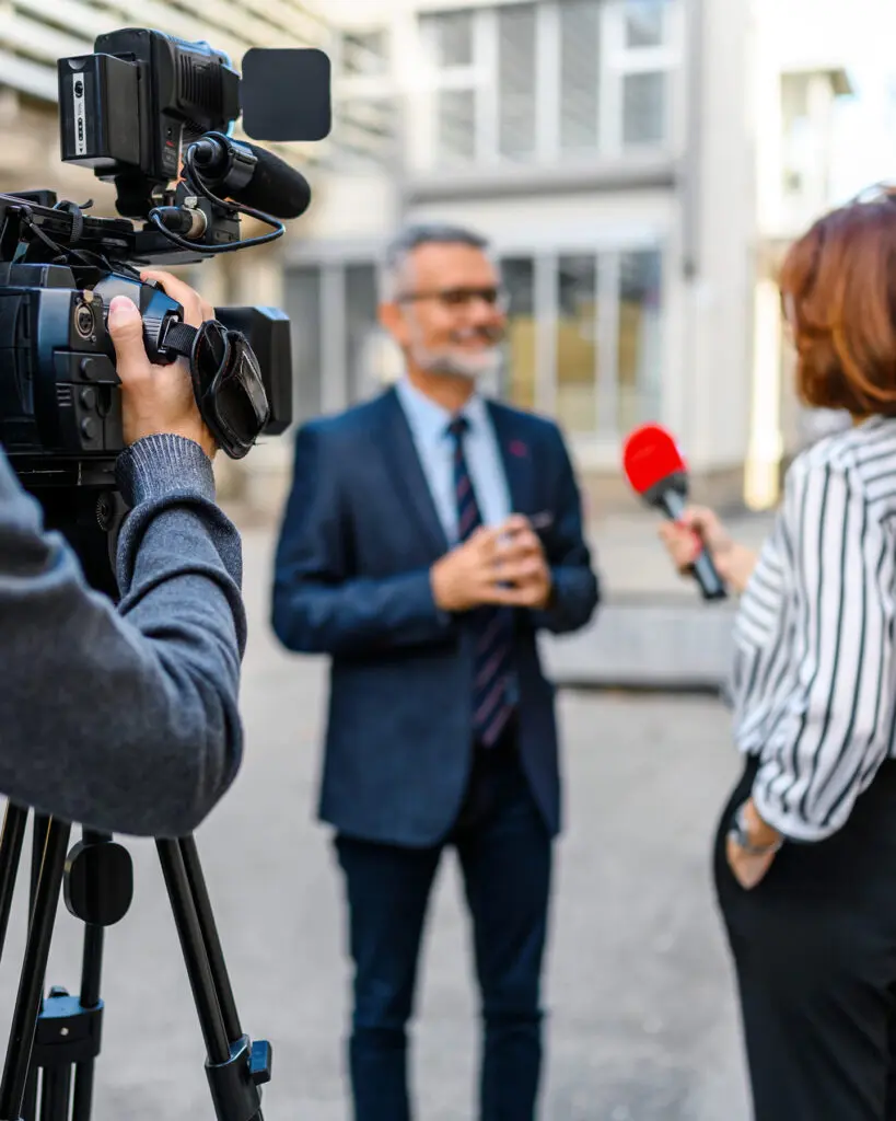 A picture of a journalist recording an interview in the streets for a public media organization.
