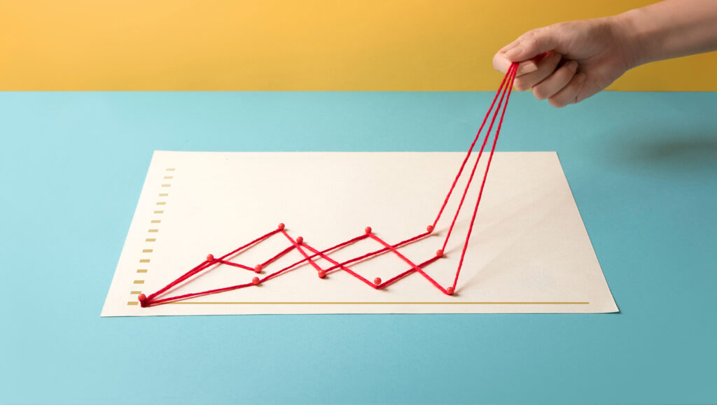 An image of a hand holding three strands of red yarn that are charting out trends on a piece of paper with thumbtacks.