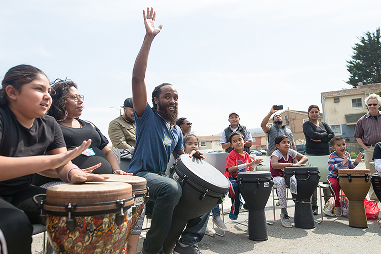 A picture of members of the San Francisco community playing djembe drums outside.