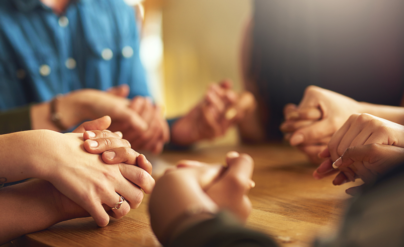 A picture of people holding hands together at a table in faith.