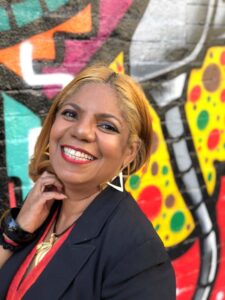 Headshot of Marietta Ulacia smiling against a mural background