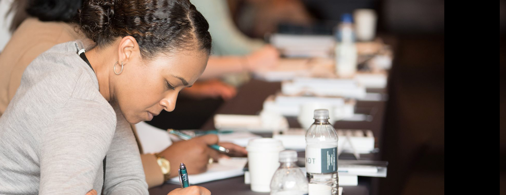 A picture of a person leaning over as they write in a notebook on a conference table.