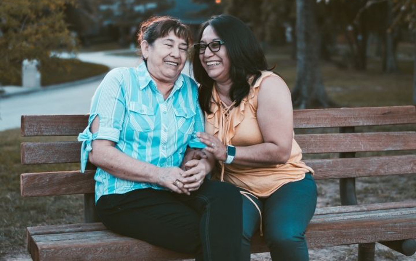 A picture of two people laughing on a bench outside.