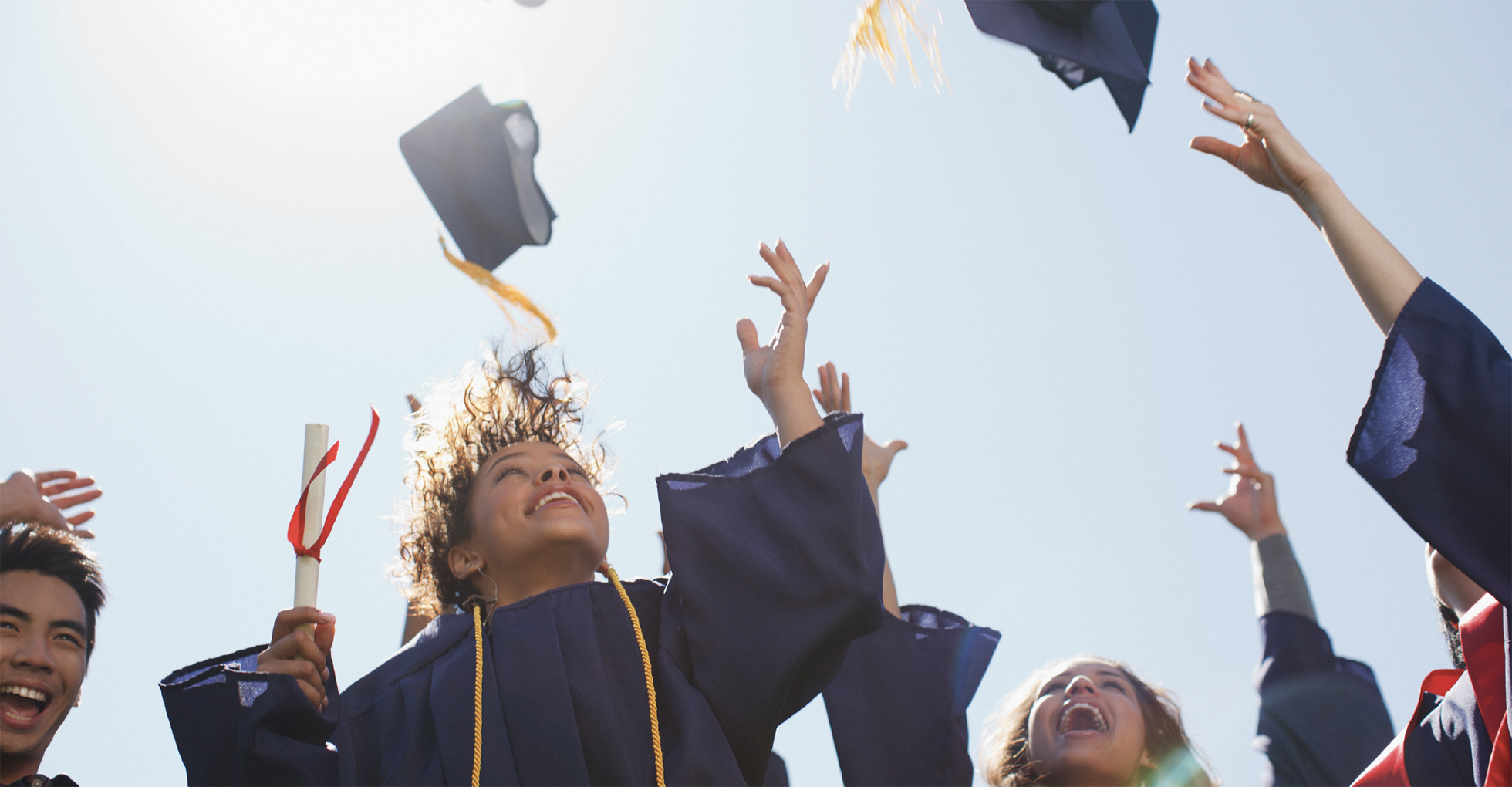 A picture of higher education graduates throwing up their caps into bluebird skies.