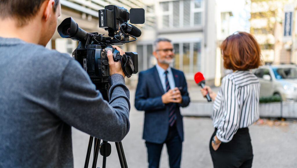 A picture of a journalist recording an interview in the streets for a public media organization.