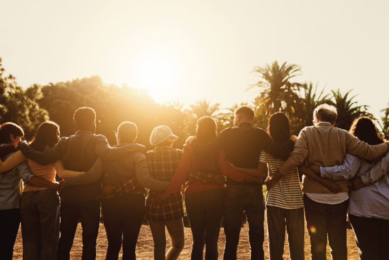 Group of people lock arms and face glowing sunset